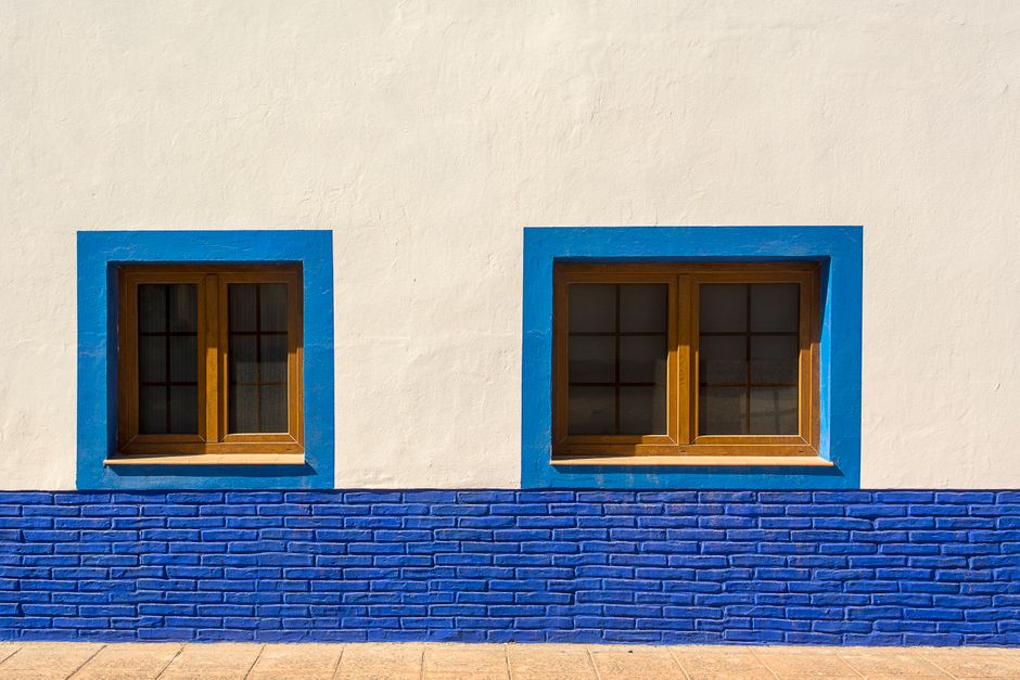 Sunlit architectural detail of blue-framed windows on a white wall showcasing modern design.
